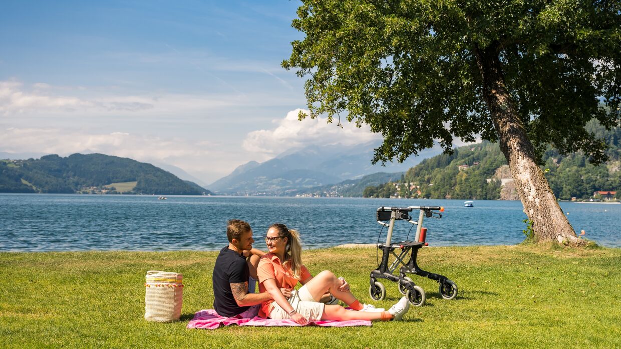 Ein Paar sitzt auf einer Picknickdecke am Ufer des Millstättersees